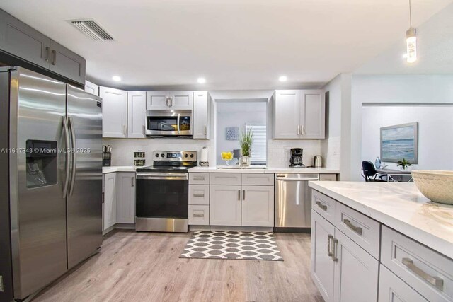 kitchen with appliances with stainless steel finishes, decorative light fixtures, sink, and light hardwood / wood-style flooring