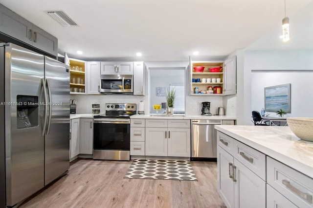 kitchen with light stone counters, gray cabinets, stainless steel appliances, light hardwood / wood-style floors, and decorative backsplash