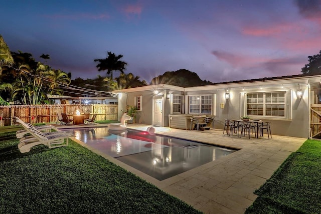 back house at dusk with a patio, a yard, and a fenced in pool