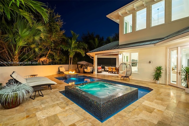 pool at twilight with a patio area, an in ground hot tub, and french doors