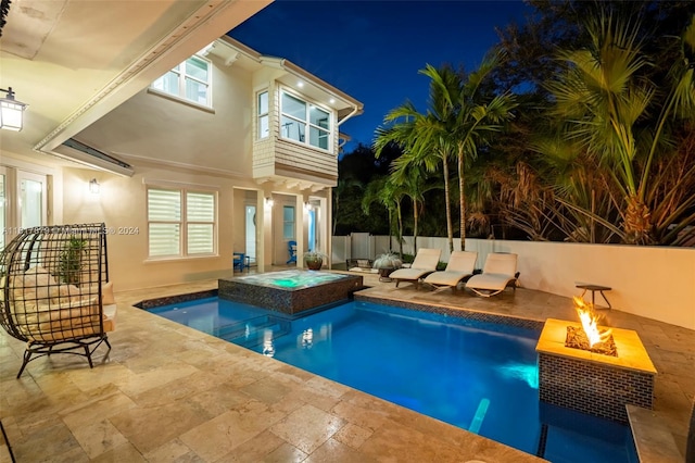 pool at night featuring an in ground hot tub, a patio, and a fire pit