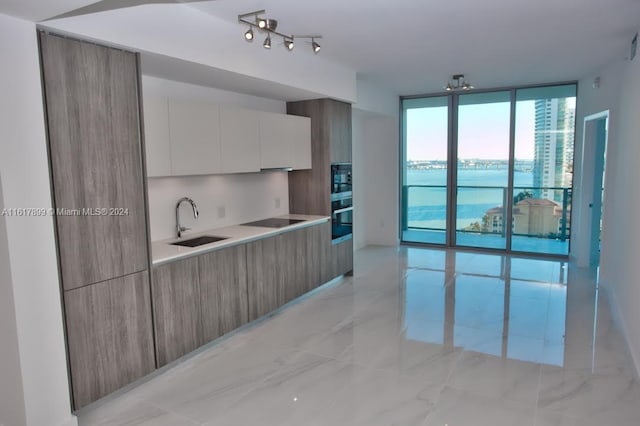 kitchen featuring stainless steel oven, sink, a water view, black electric cooktop, and white cabinets