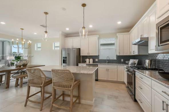 kitchen with light tile patterned flooring, pendant lighting, decorative backsplash, a center island, and high end appliances