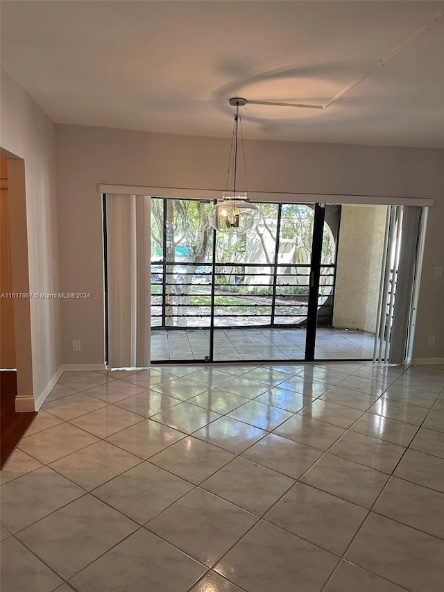 tiled empty room with plenty of natural light and a chandelier