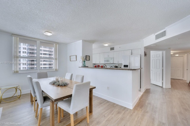 dining space with a textured ceiling and light hardwood / wood-style flooring