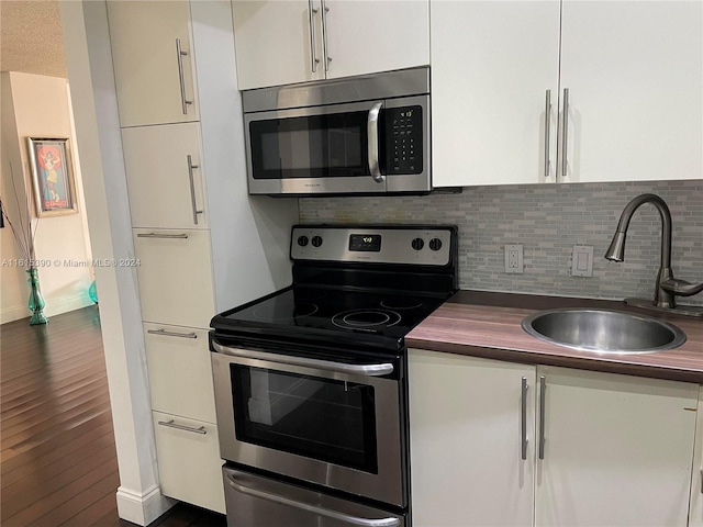 kitchen with tasteful backsplash, stainless steel appliances, white cabinets, sink, and dark wood-type flooring