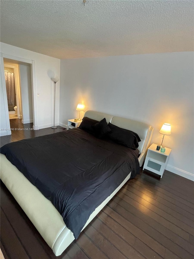 bedroom featuring ensuite bath, dark hardwood / wood-style floors, and a textured ceiling