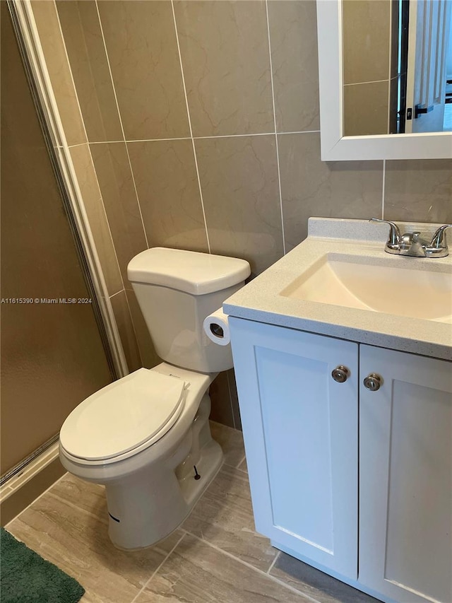 bathroom featuring vanity, toilet, an enclosed shower, and tile walls