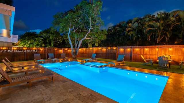 pool at night featuring a patio area and an in ground hot tub