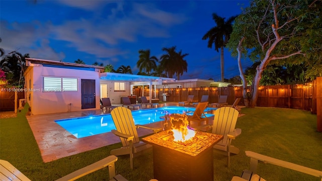 pool at dusk with an outdoor fire pit, a yard, and a patio