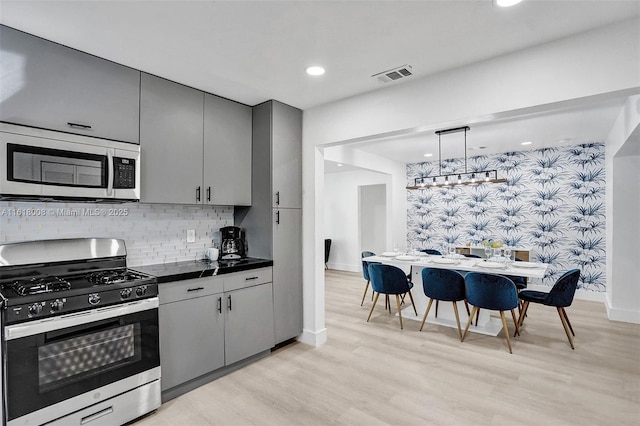 kitchen featuring gray cabinets, decorative light fixtures, tasteful backsplash, stainless steel appliances, and light hardwood / wood-style flooring