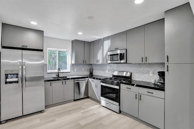 kitchen with appliances with stainless steel finishes, sink, gray cabinetry, decorative backsplash, and light wood-type flooring