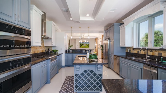 kitchen featuring wall chimney range hood, backsplash, a kitchen island, a tray ceiling, and stainless steel appliances