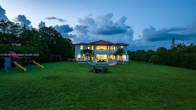 back of property featuring a playground, a balcony, and a lawn