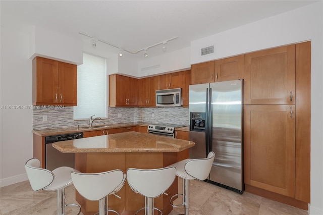 kitchen featuring sink, a center island, tasteful backsplash, light stone counters, and appliances with stainless steel finishes