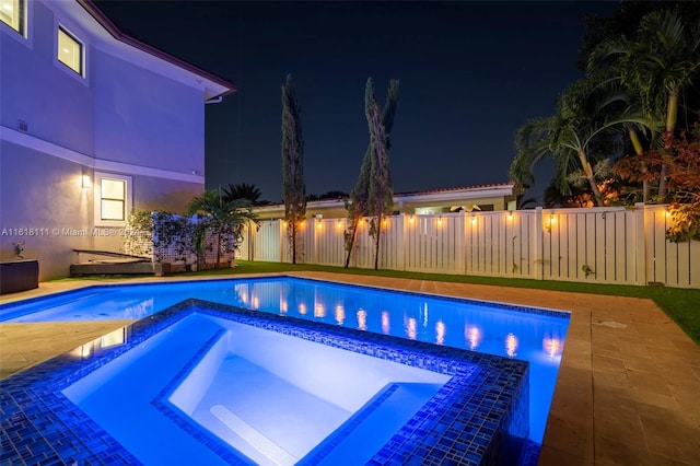 pool at twilight featuring an in ground hot tub