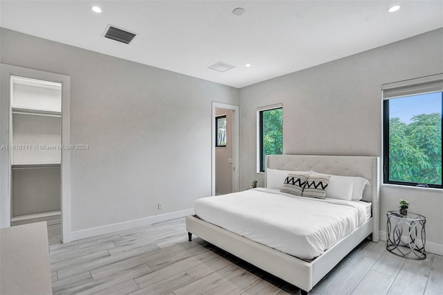 bedroom featuring multiple windows, a spacious closet, and light hardwood / wood-style floors