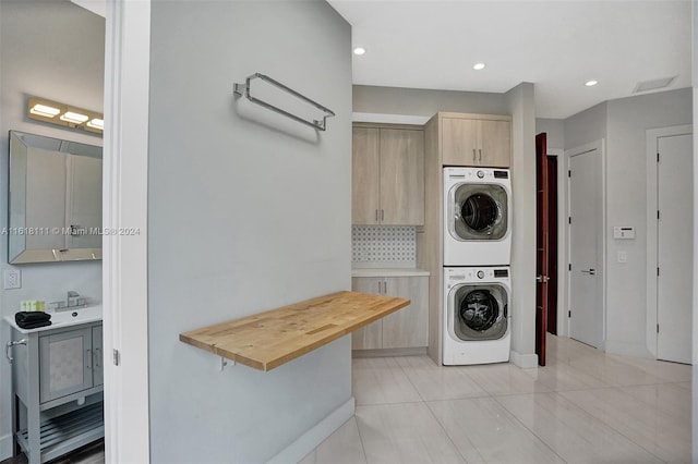 laundry area with cabinets, stacked washer / drying machine, and light tile patterned floors