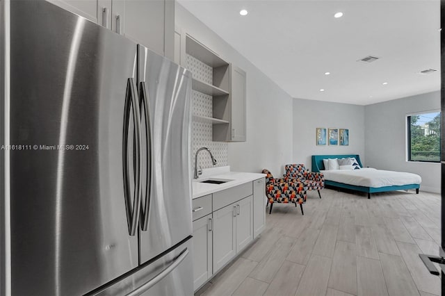 kitchen featuring light hardwood / wood-style flooring, sink, white cabinetry, stainless steel fridge, and decorative backsplash