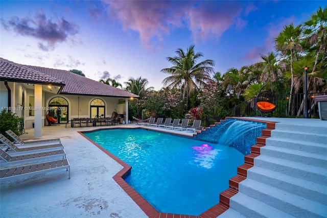 pool at dusk with a patio and pool water feature