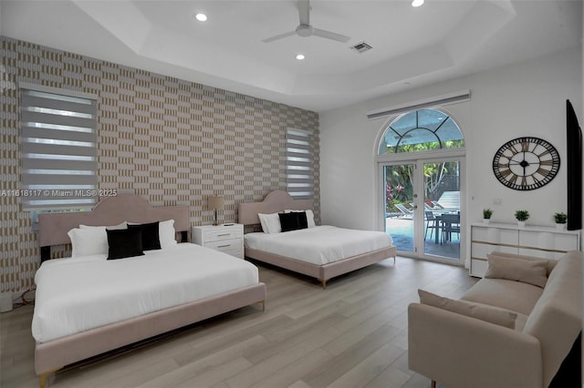 bedroom featuring ceiling fan, access to outside, light hardwood / wood-style floors, and a tray ceiling