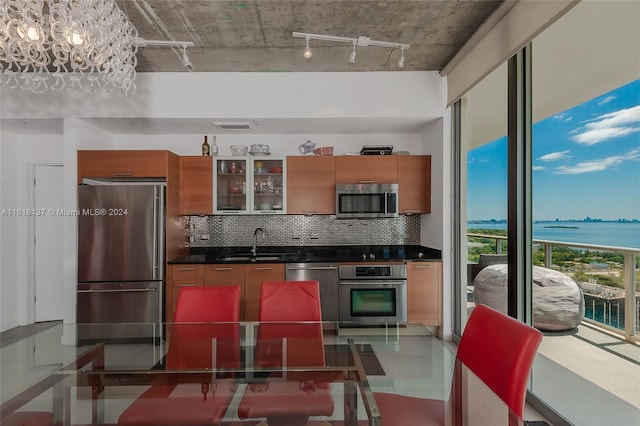 kitchen featuring dark countertops, appliances with stainless steel finishes, glass insert cabinets, a water view, and a sink