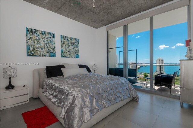 bedroom featuring a water view, expansive windows, access to outside, and tile patterned floors