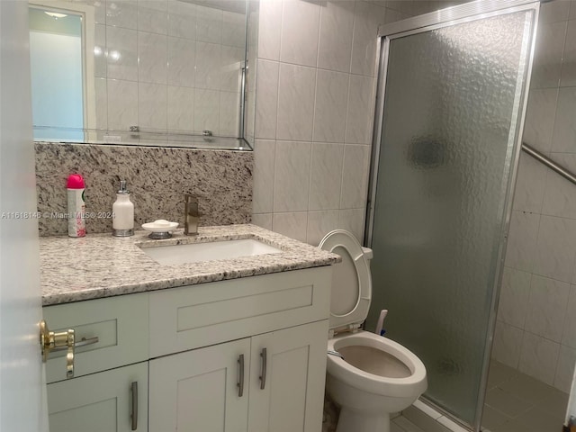 bathroom featuring vanity, tasteful backsplash, tile walls, a shower with shower door, and toilet