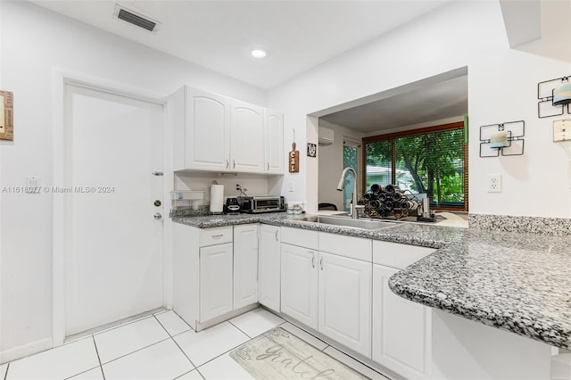 kitchen featuring an AC wall unit, dark stone counters, light tile patterned floors, sink, and white cabinets