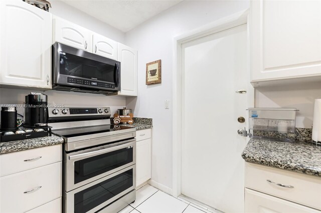 kitchen featuring white cabinets, light tile patterned flooring, dark stone counters, and appliances with stainless steel finishes