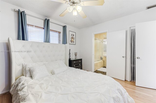 bedroom featuring ceiling fan, ensuite bath, light hardwood / wood-style flooring, and a textured ceiling