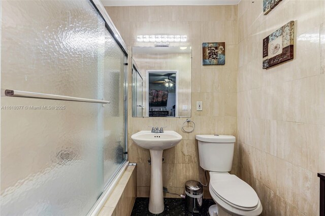 full bathroom with tile walls, shower / bath combination with glass door, sink, toilet, and ceiling fan