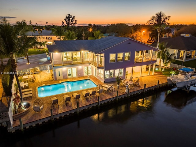 back house at dusk with a water view, a balcony, a fenced in pool, and a patio area