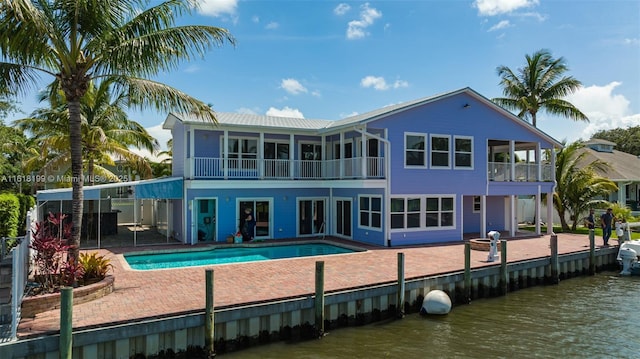 back of property with a water view, a sunroom, a fenced in pool, and a patio area