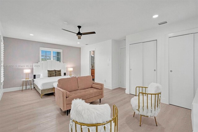 bedroom with ceiling fan, light hardwood / wood-style floors, and two closets