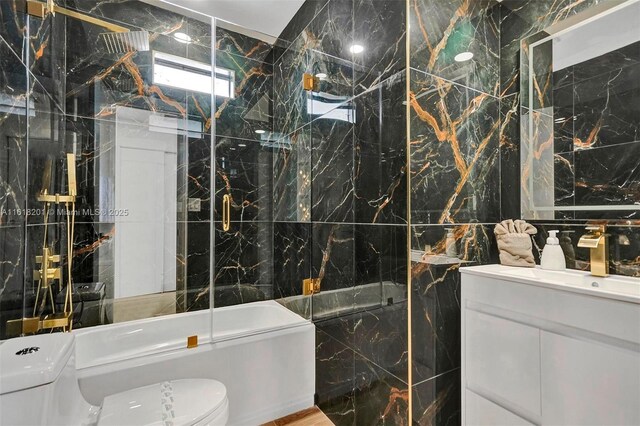 full bathroom with tile walls, combined bath / shower with glass door, vanity, and toilet