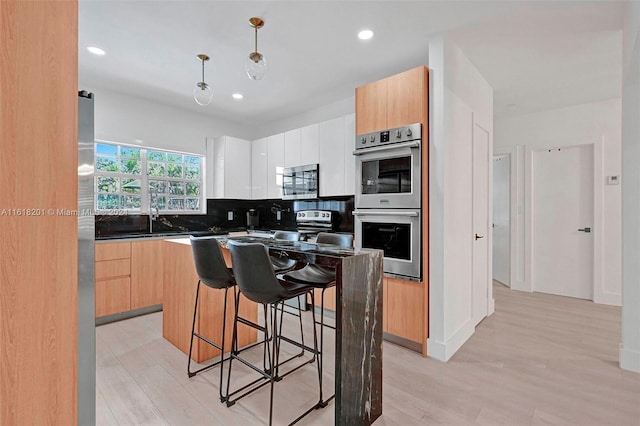 kitchen with decorative light fixtures, tasteful backsplash, white cabinetry, a kitchen island, and stainless steel appliances