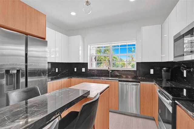 kitchen with white cabinetry, stainless steel appliances, dark stone countertops, decorative backsplash, and sink