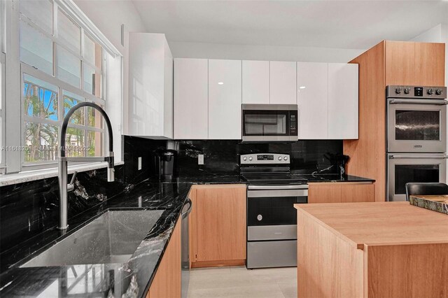 kitchen with sink, tasteful backsplash, white cabinetry, dark stone countertops, and stainless steel appliances