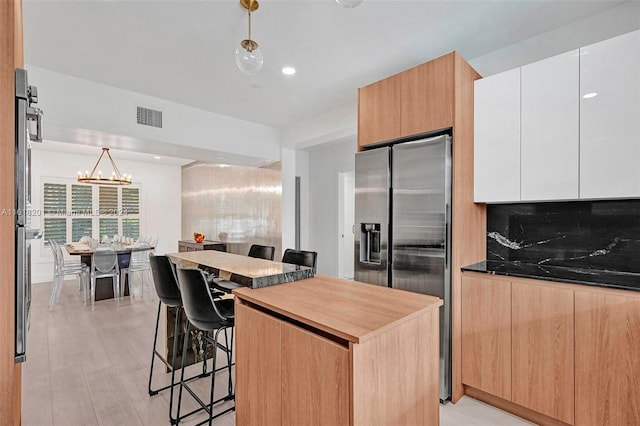 kitchen featuring decorative light fixtures, white cabinets, decorative backsplash, stainless steel fridge with ice dispenser, and a breakfast bar area