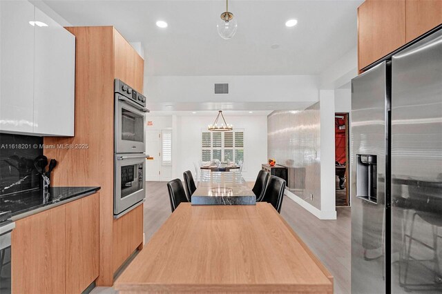 kitchen featuring pendant lighting, light hardwood / wood-style floors, white cabinetry, and appliances with stainless steel finishes