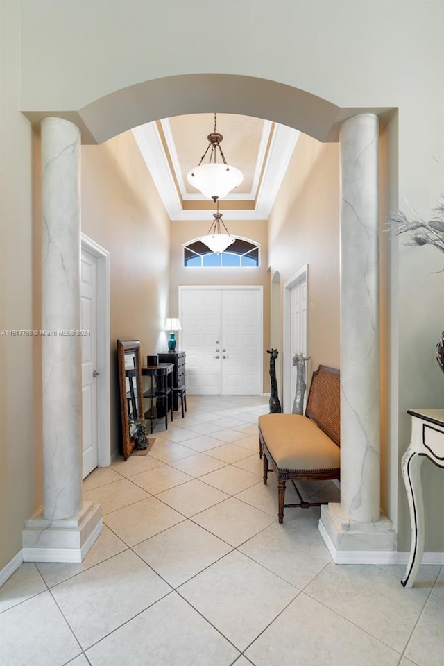 entryway featuring a towering ceiling, ornamental molding, light tile patterned floors, and a tray ceiling