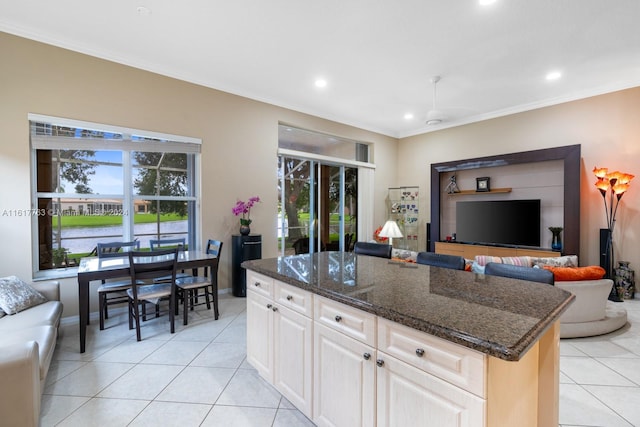 kitchen with dark stone counters, crown molding, light tile patterned floors, a water view, and a kitchen island