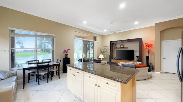 kitchen with white cabinetry, ceiling fan, a center island, dark stone countertops, and light tile patterned floors