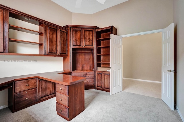 unfurnished office featuring ceiling fan, light colored carpet, and built in desk