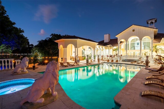 pool at twilight featuring a patio and an in ground hot tub