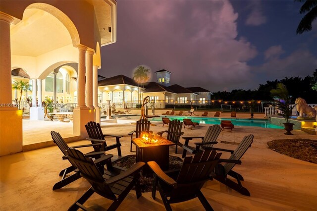 patio at twilight with a fire pit and a community pool