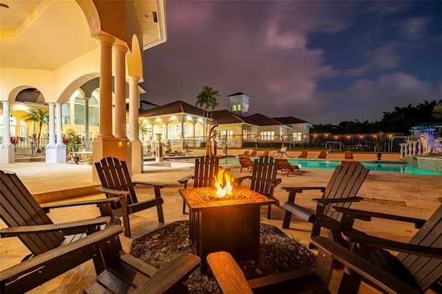 patio at night featuring an outdoor fire pit and a fenced in pool