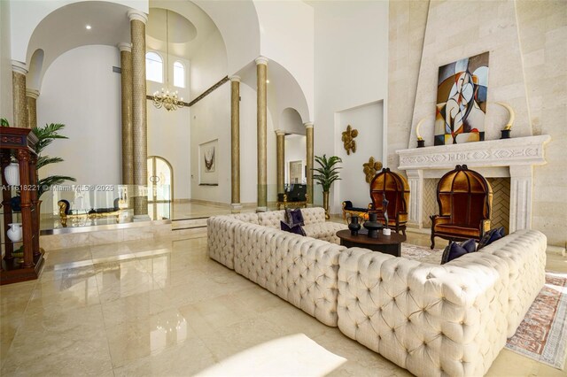 tiled living room featuring ornate columns, a chandelier, a high end fireplace, and a high ceiling