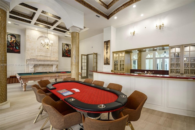 game room with ornate columns, a fireplace, a high ceiling, coffered ceiling, and light hardwood / wood-style floors